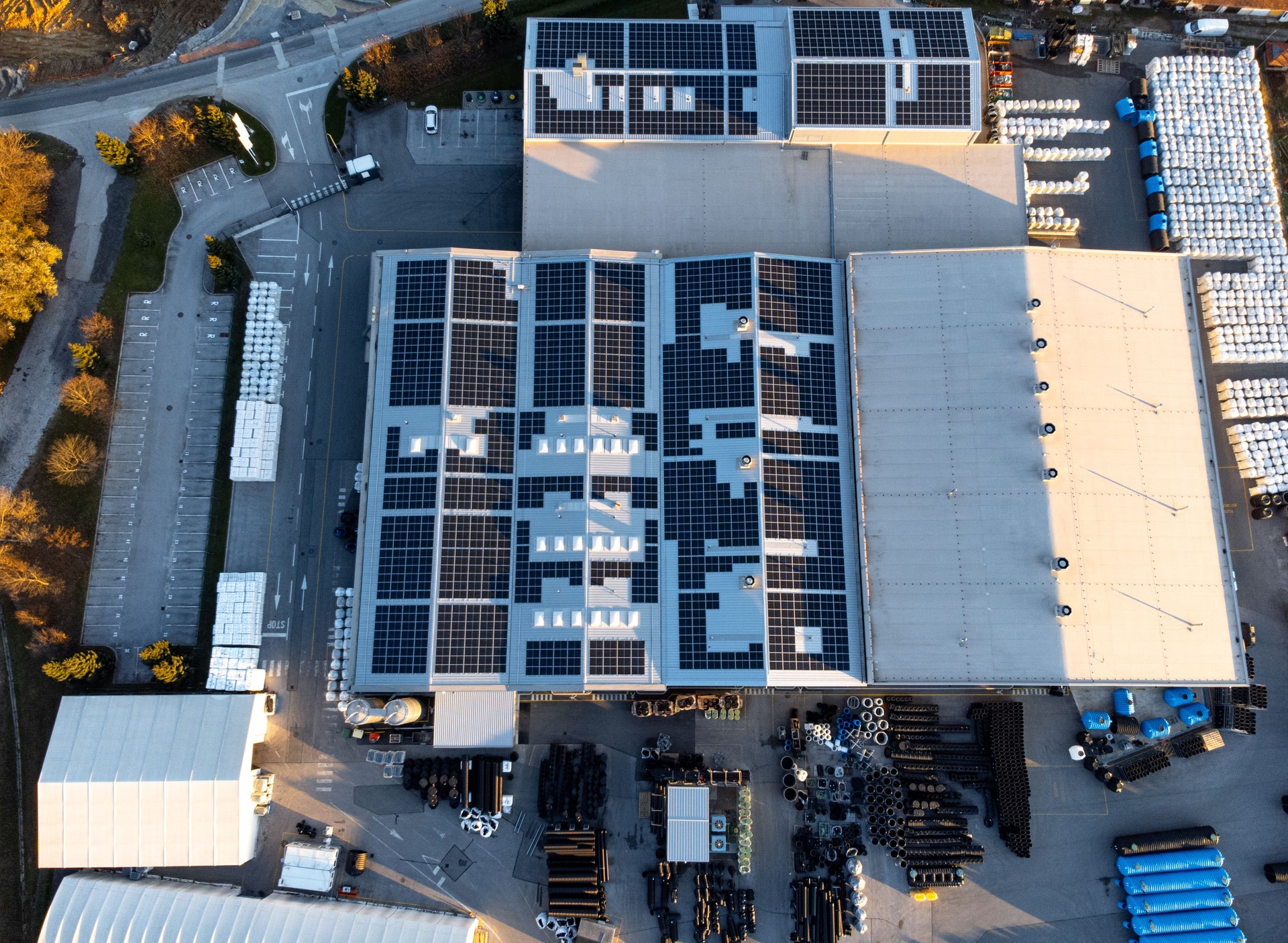 Factory building producing plastic pipes with large array of solar panels on the roof at sunset top down